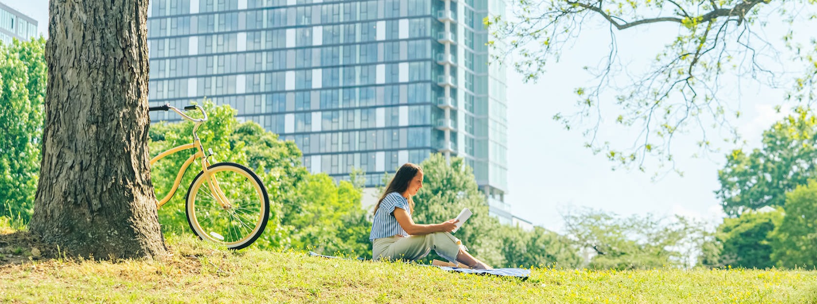 woman reading in a park with her bicycle leaning against a tree